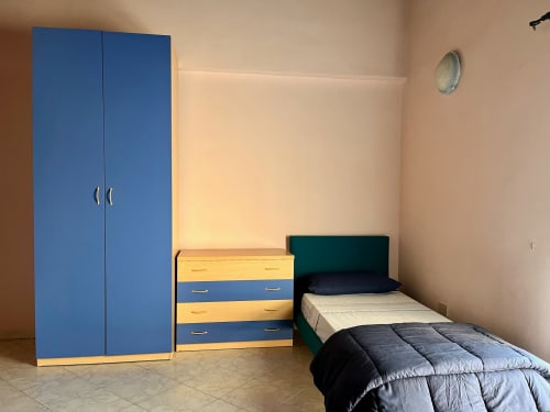 Camera da letto dell'Aparthotel Tirreno con armadio blu, cassettone giallo e blu, letto singolo con coperta scura, Tirrenia