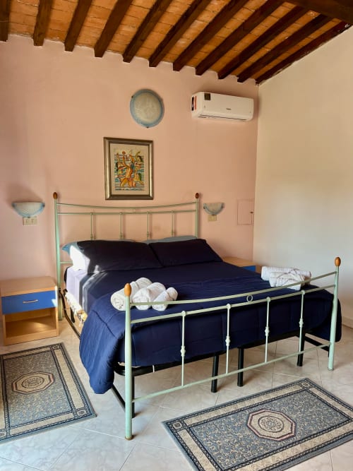 Camera luminosa nell'Appartamento Tirreno, Tirrenia con letto in metallo verde menta, biancheria blu navy, travi in legno e aria