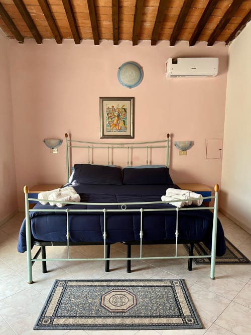 Camera da letto dell'Appartamento Tirreno a Tirrenia con letto in metallo verde menta, biancheria blu navy, pareti rosa, soffitto con travi in legno