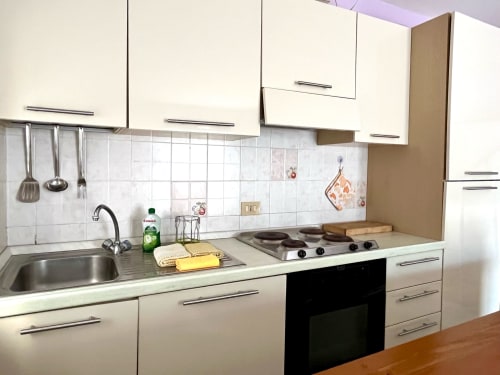 Cucina moderna dell'Apartment Tirreno con cabinetry bianca, fornello, lavello e rivestimento in piastrelle a Tirrenia