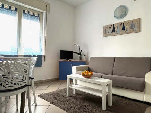 Soggiorno moderno all'Apartment Tirreno a Tirrenia con divano grigio, tavolino bianco, mobile TV blu e arredi nautici.