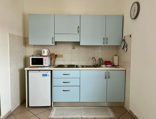 Cucina compatta in Apartment Tirreno, Tirrenia con armadi azzurri, microonde, piano cottura e piccolo frigorifero