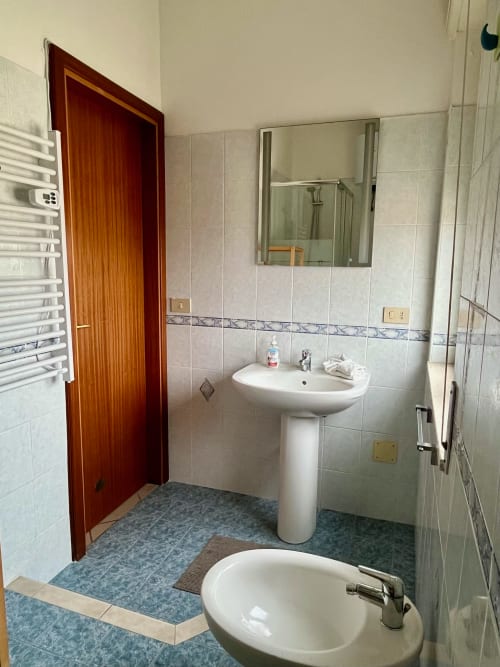 Bagno dell'Appartamento Tirreno a Tirrenia con lavabo a colonna, specchio, box doccia e pavimenti piastrellati
