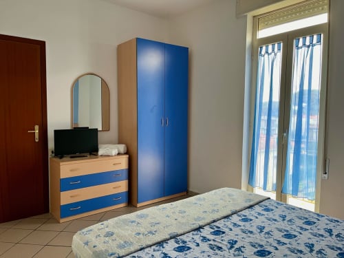 Camera moderna dell'Apartment Tirreno a Tirrenia con armadio blu, scrivania con TV e biancheria floreale