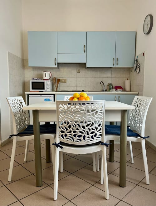 Moderna zona cucina-pranzo con sedie bianche decorate, tavolo con agrumi, armadi blu e microonde in Appartamento