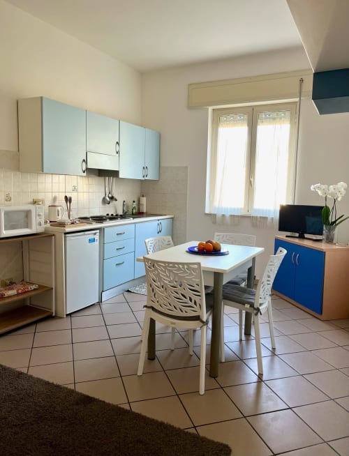 Moderna zona cucina-soggiorno dell'Apartment Tirreno a Tirrenia con mobili blu, tavolo da pranzo e TV