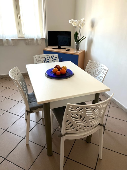Zona pranzo dell'Appartamento Tirreno con tavolo bianco, sedie con motivi floreali e ciotola di frutta fresca a Tirrenia