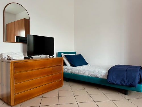 Camera da letto moderna presso l'Apartment Tirreno a Tirrenia con letto turchese, cassettone in legno, TV e specchio ad arco