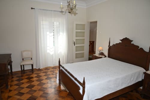 Quarto elegante na Villa Sor em Ponte de Sor com cama de madeira antiga, roupa de cama branca, piso de tacos e luz natural