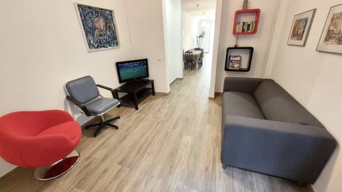 Mira Barna Barcelona apartment sitting area with red chair, gray sofa, TV, and artwork on walls