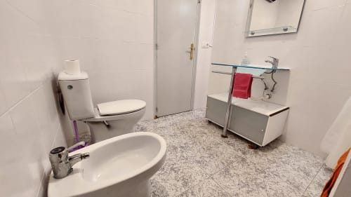 Modern bathroom in Barcelona apartment with toilet, sink, and vanity. Clean white tile walls and gray speckled flooring.