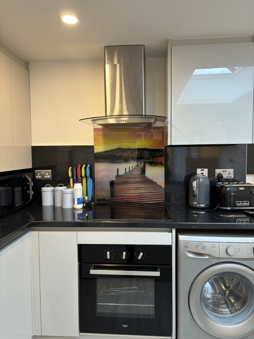 Modern kitchen with black granite countertops, white cabinetry, stainless steel range hood, oven, and washing machine at