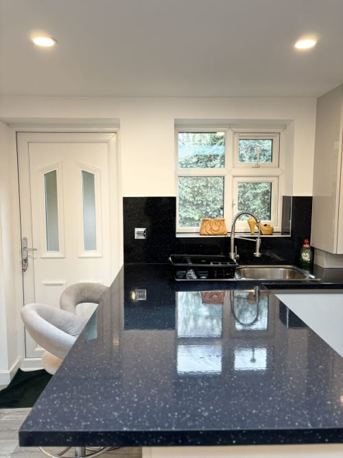 Modern kitchen with black speckled counters, stainless steel sink, white cabinets, garden view windows, and curved chair at