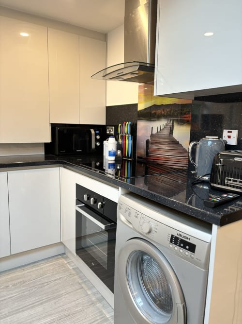 Modern kitchen with white cabinets, black countertop, washing machine, oven, and stainless steel hood at CozyNest villa in