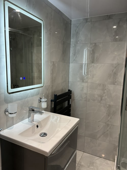 Modern bathroom with LED mirror, white sink, marble tiles, and walk-in shower at CozyNest villa in High Wycombe