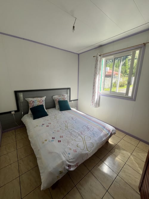 Chambre de l'hôtel Au pied des Sources à Cilaos avec lit, oreillers, vue sur la fenêtre et carrelage