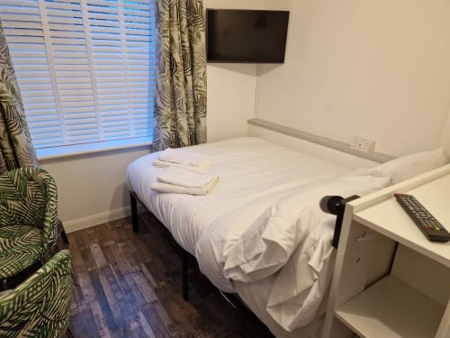 Modern hotel bedroom at The Little Annex in Horsham with white bed, desk, TV, patterned curtains and wooden flooring.