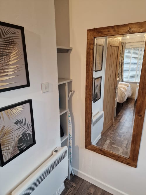 Modern apartment hallway at The Little Annex Horsham with wooden mirror, palm leaf artwork, and open doorway to bedroom