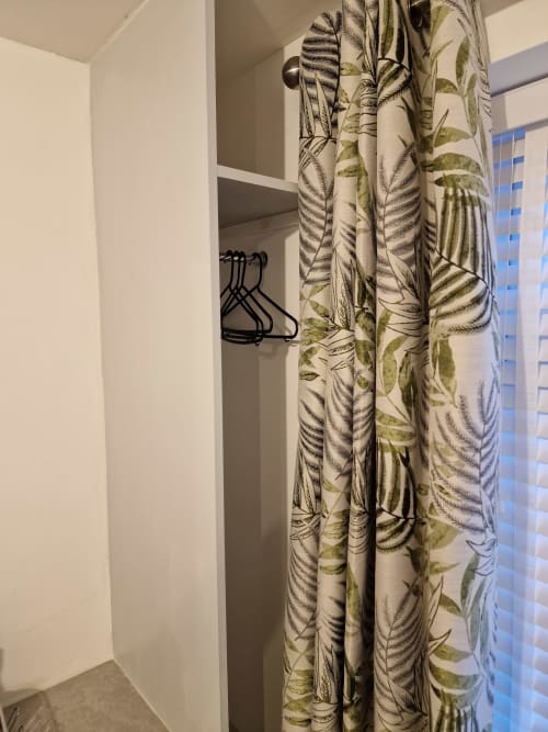 Wardrobe closet with botanical patterned curtain and black hangers in The Little Annex apartment, Horsham