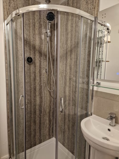 Modern curved shower enclosure with grey wood-effect tiles and rainfall showerhead in The Little Annex apartment, Horsham