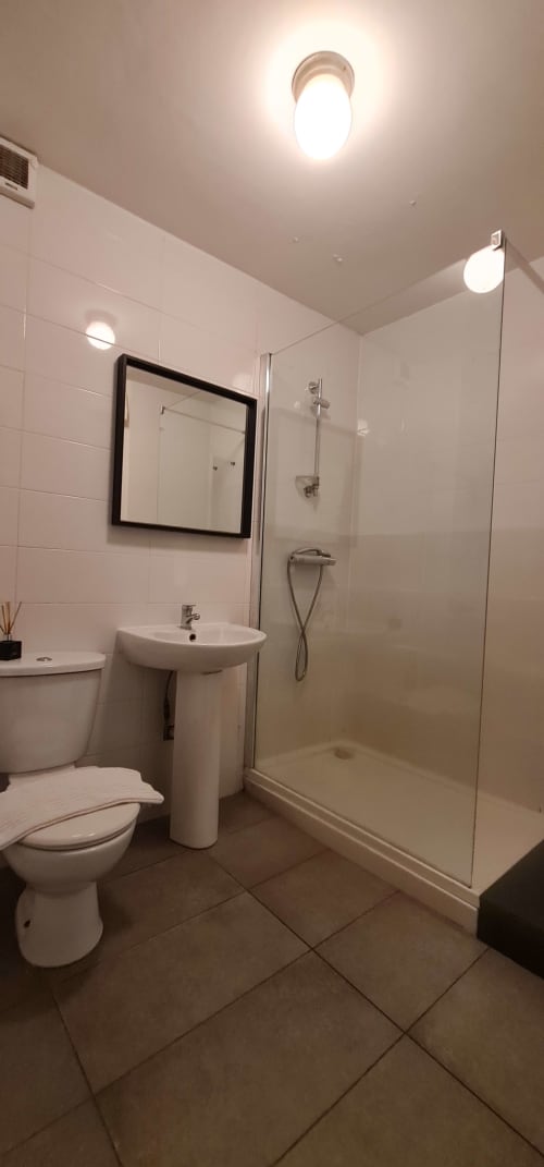 Modern bathroom at Dublin Exchange Suites with white tiles, pedestal sink, mirror, walk-in shower, toilet, and bright ceiling