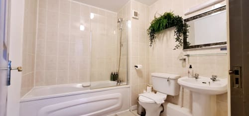 Modern bathroom in Dublin Exchange Suites apartment with bathtub, toilet, pedestal sink, and decorative hanging plants