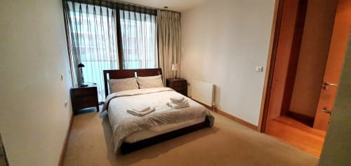 Master bedroom in Dublin Exchange Suites 2-bedroom apartment with river view, queen bed, balcony access, and hardwood floors