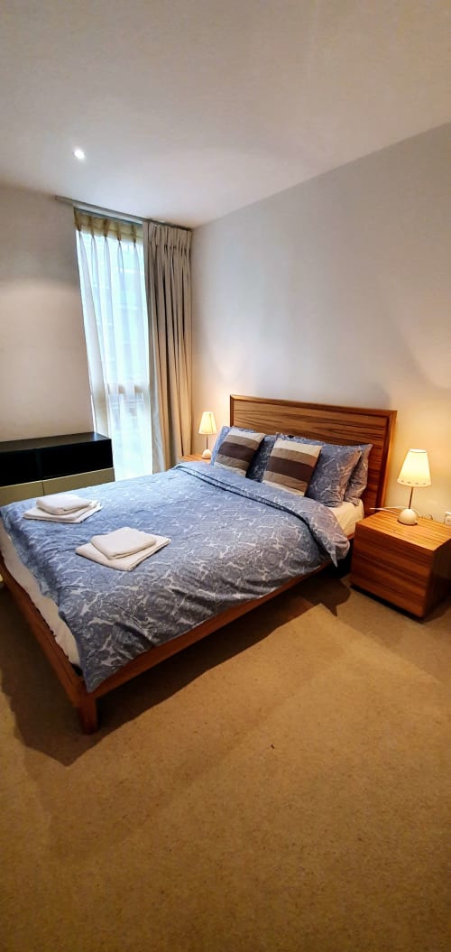 Modern bedroom at Dublin Exchange Suites with wooden bed, blue bedding, twin lamps, curtains, and carpet flooring