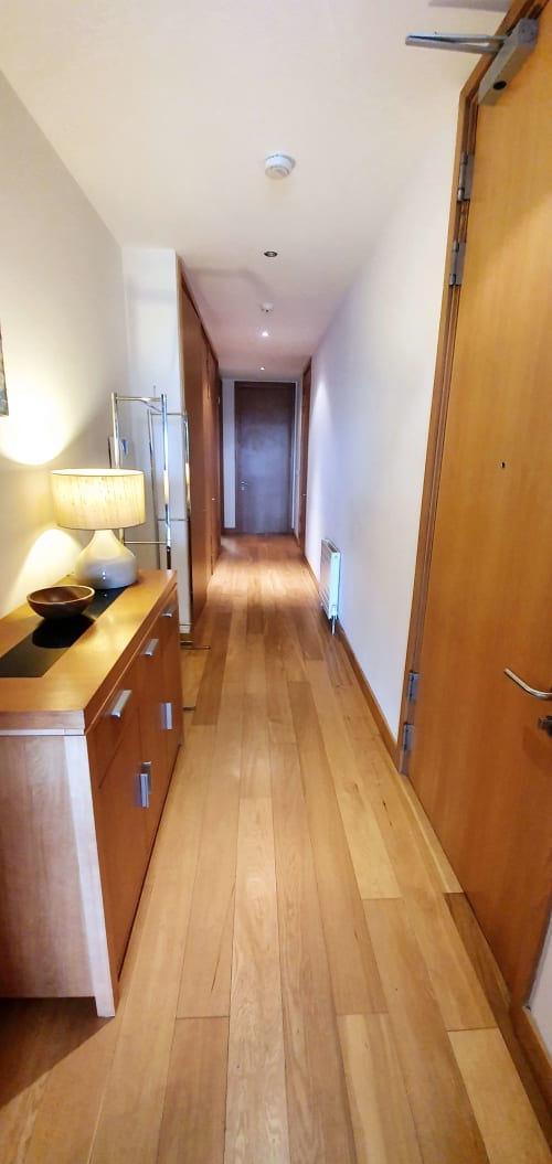 Modern hallway in Dublin Exchange Suites apartment with wooden floors, white walls, and wood cabinetry with lamp lighting