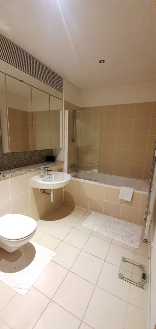 Modern bathroom in Dublin Exchange Suites 2-bedroom apartment with toilet, sink, mirror, bathtub, and shower enclosure