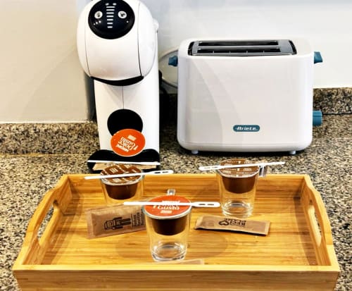 Cafetera y tostadora en encimera de granito con bandeja de madera con cápsulas de café