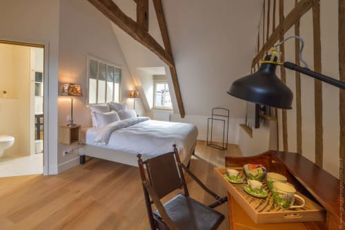 Spacious loft bedroom in Honfleur cottage with exposed wooden beams, white bedding, wooden desk with chair, black pendant