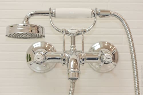 Chrome shower and bath faucet with dual handles, overhead rainfall showerhead, and handheld shower spray at cottage in