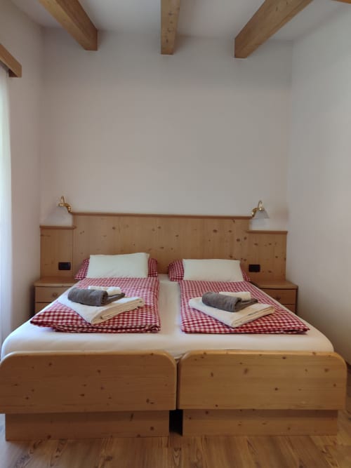 Twin beds with red checkered bedding and wooden headboard in Sassolungo Apartment at Residence Rodolon, Mazzin