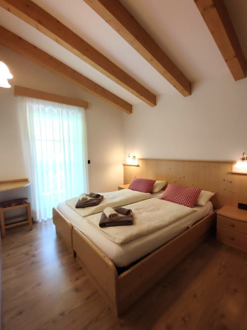 Cozy bedroom with wooden beams, queen bed, red checkered pillows, and alpine views at Residence Rodolon
