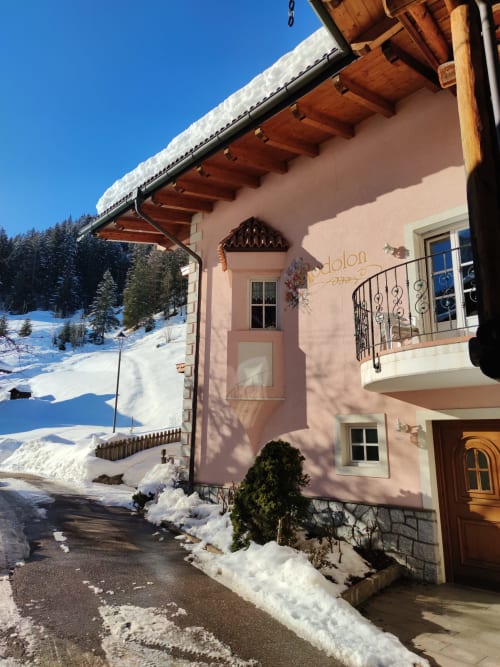 Residence Rodolon alpines Chalet im verschneiten Mazzin mit Holzbalkonen und klarem blauen Himmel