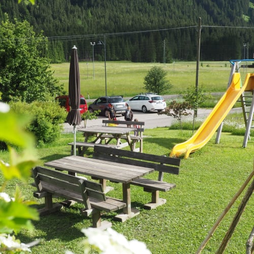 Spielplatz mit Picknicktischen und gelber Rutsche bei Residence Rodolon in Mazzin, umgeben von Wald und geparkten Autos