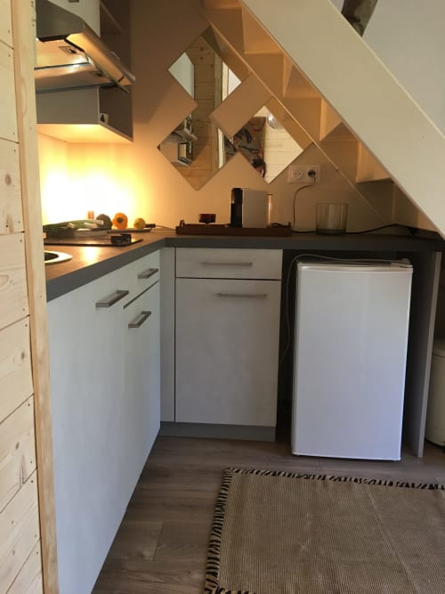 Compact kitchen in The Nest cottage at Clairseine B&B with white cabinets, dark countertop, small refrigerator, and angled