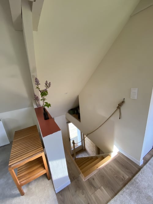 Staircase in The Nest cottage at Clairseine B&B with wooden steps, modern railing, and purple flowers on wooden bench