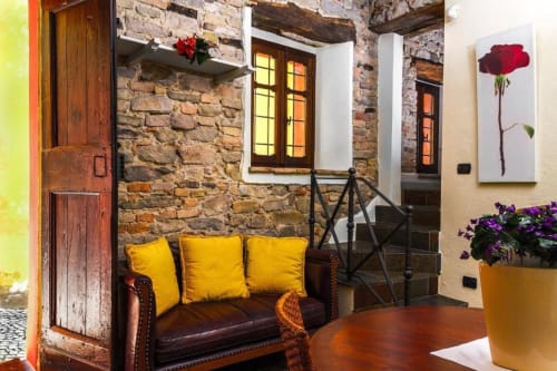 Entrée rustique en pierre de l'appartement Dimora i Manichei à Monforte d'Alba avec canapé cuir, coussins jaunes et fleurs