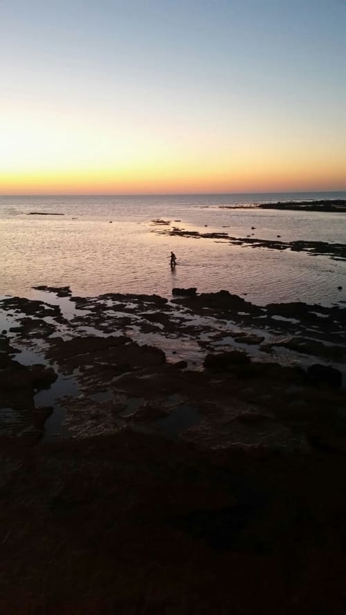 Sunset at Bungalow Buda Beach in Chipiona with rocky coastline and solitary swimmer in golden hour light