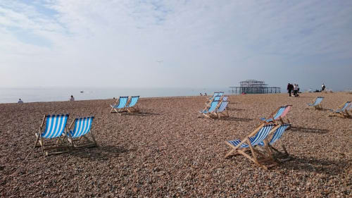 Blue and white striped deckchairs on pebbly beach with sea and pier ruins visible
