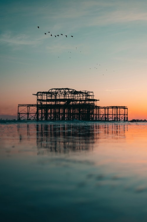 Abandoned West Pier at sunset reflecting in shallow water with birds flying overhead near Horsham
