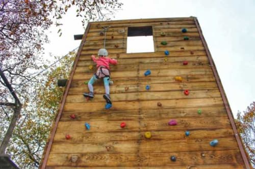 Criança escalando parede de madeira com pranchas coloridas no parque de aventura Casa da Luz Gerês em Vieira do Minho