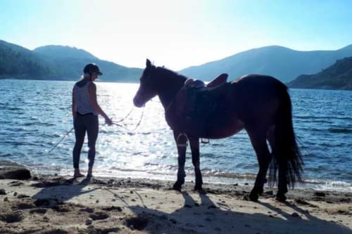 Pessoa com cavalo escuro na praia da Casa da Luz Gerês, montanhas e lago ao fundo, Vieira do Minho