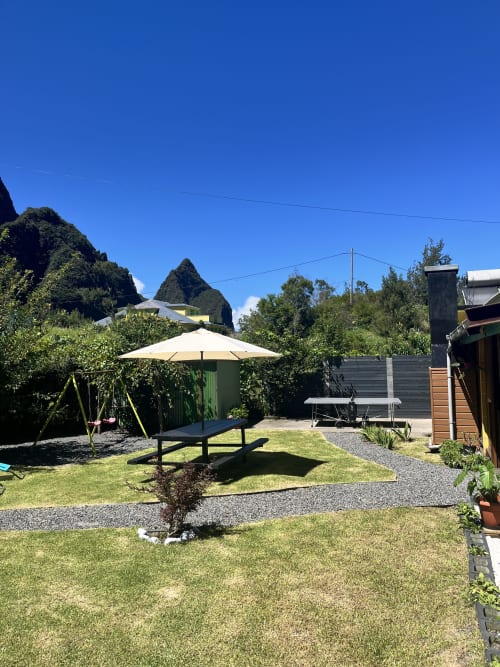 Jardin d'Au pied des Sources avec table de pique-nique, parasol et pelouse verdoyante à Cilaos