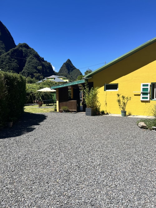 Bungalow jaune éclatant à Au pied des Sources à Cilaos avec cour en gravier et impressionnante toile de fond montagneuse