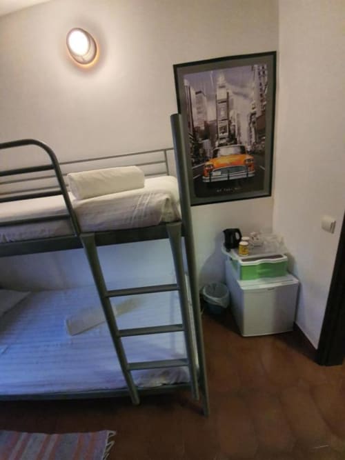 Economy bunk bed room at Ocean View Lagos hostel with metal frame beds, white bedding, fridge, and NYC taxi poster in Lagos.