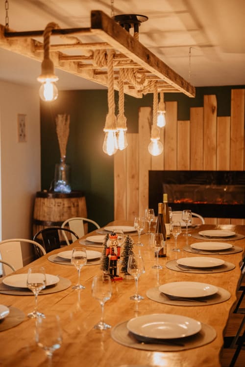 Élégante salle à manger du Repaire Des Darous avec table en bois, couverts, luminaires suspendus en corde et cheminée