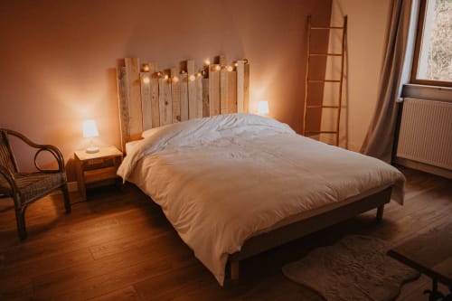 Chambre douillette au Gîte Repaire Des Darous avec tête de lit en bois rustique, éclairage chaleureux et parquet à Saulxures sur